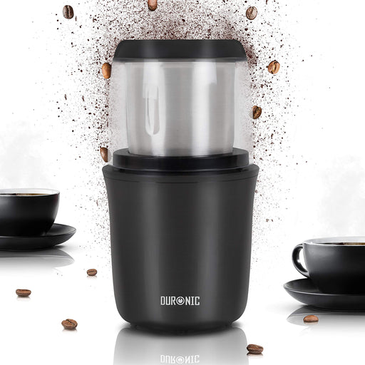 Duronic CG250 Molinillo de Café Eléctrico 250 W, Capacidad para 75 g | Mostrando el molinillo de café eléctrico en color negro con un recipiente superior transparente y tazas de café a los lados con granos y café molido dispersos decorativamente