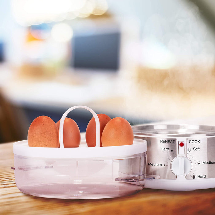 Duronic EB35 WE Hervidor para huevos eléctrico | Mostrando el hervidor de huevos eléctrico con su base de acero inoxidable y la tapa transparente colocada a un lado sobre la mesa, mientras la bandeja interior con asa sostiene los huevos listos para su cocción