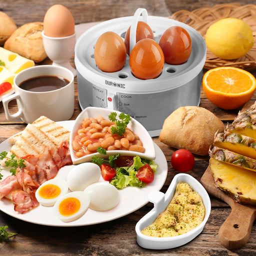 Duronic EB35 WE Hervidor para huevos eléctrico | Mostrando el hervidor de huevos eléctrico sobre una mesa de desayuno llena de alimentos, con huevos colocados en su bandeja soporte superior sin la tapa, acompañado de platos con bacon, tostadas, frijoles y accesorios para pochar con preparaciones de huevo