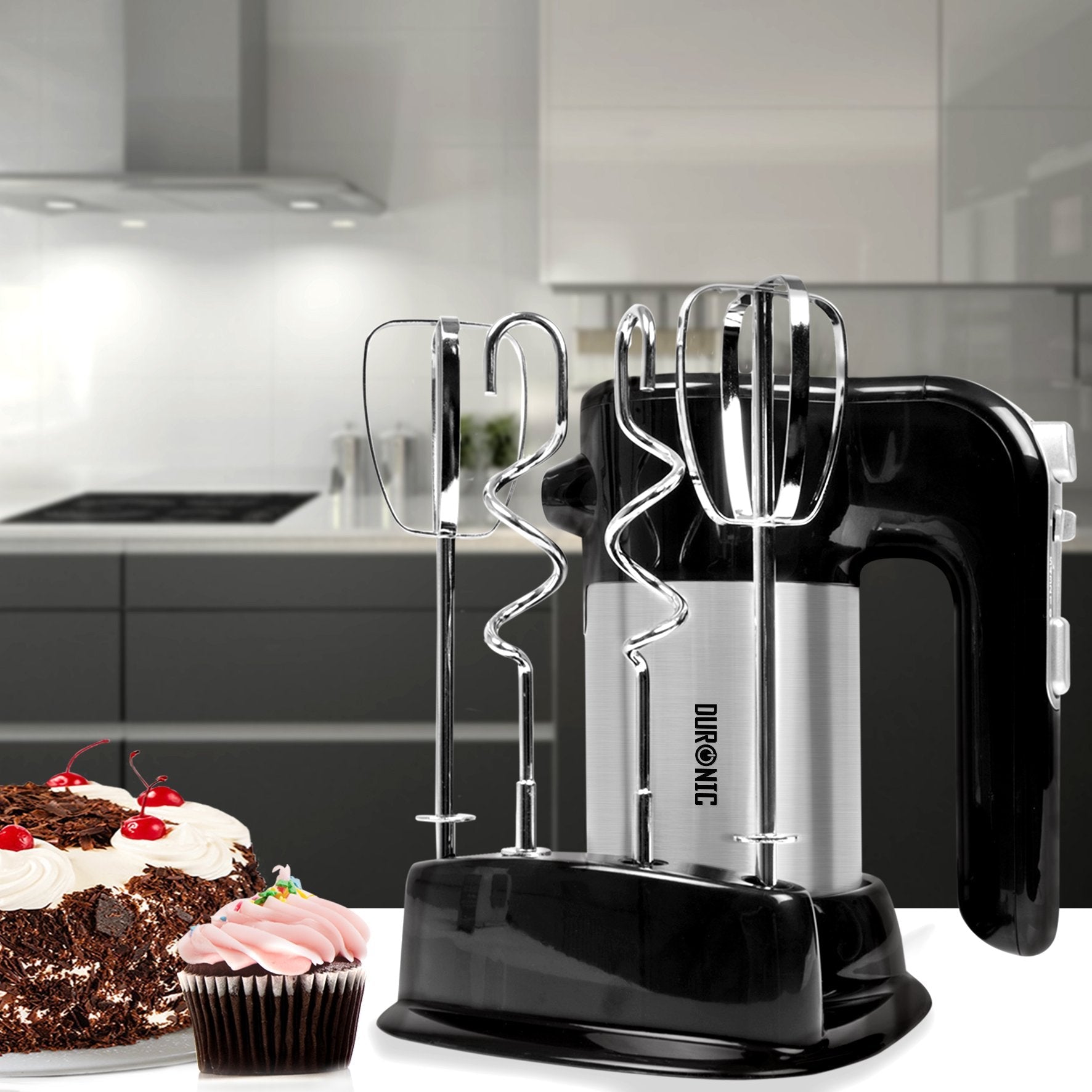Duronic HM3 Batidora Amasadora Eléctrica Mostrando la batidora de repostería guardada con sus ganchos y varillas en la base de almacenamiento, junto a una tarta de chocolate y un cupcake decorados