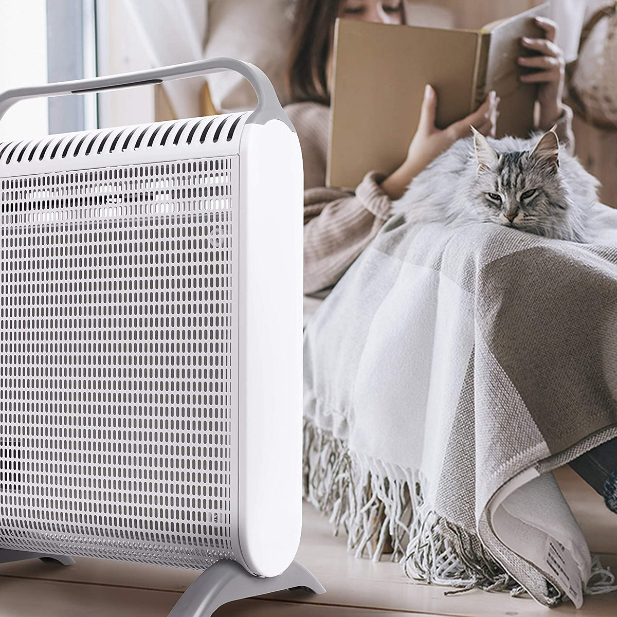 Duronic HV180 Radiador Eléctrico Compacto con Paneles de Mica 1800 W | Mostrando un primer plano del radiador de mica en color blanco y gris en un ambiente acogedor junto a una ventana, donde una persona lee un libro en segundo plano y un gato descansa plácidamente sobre una manta a cuadros