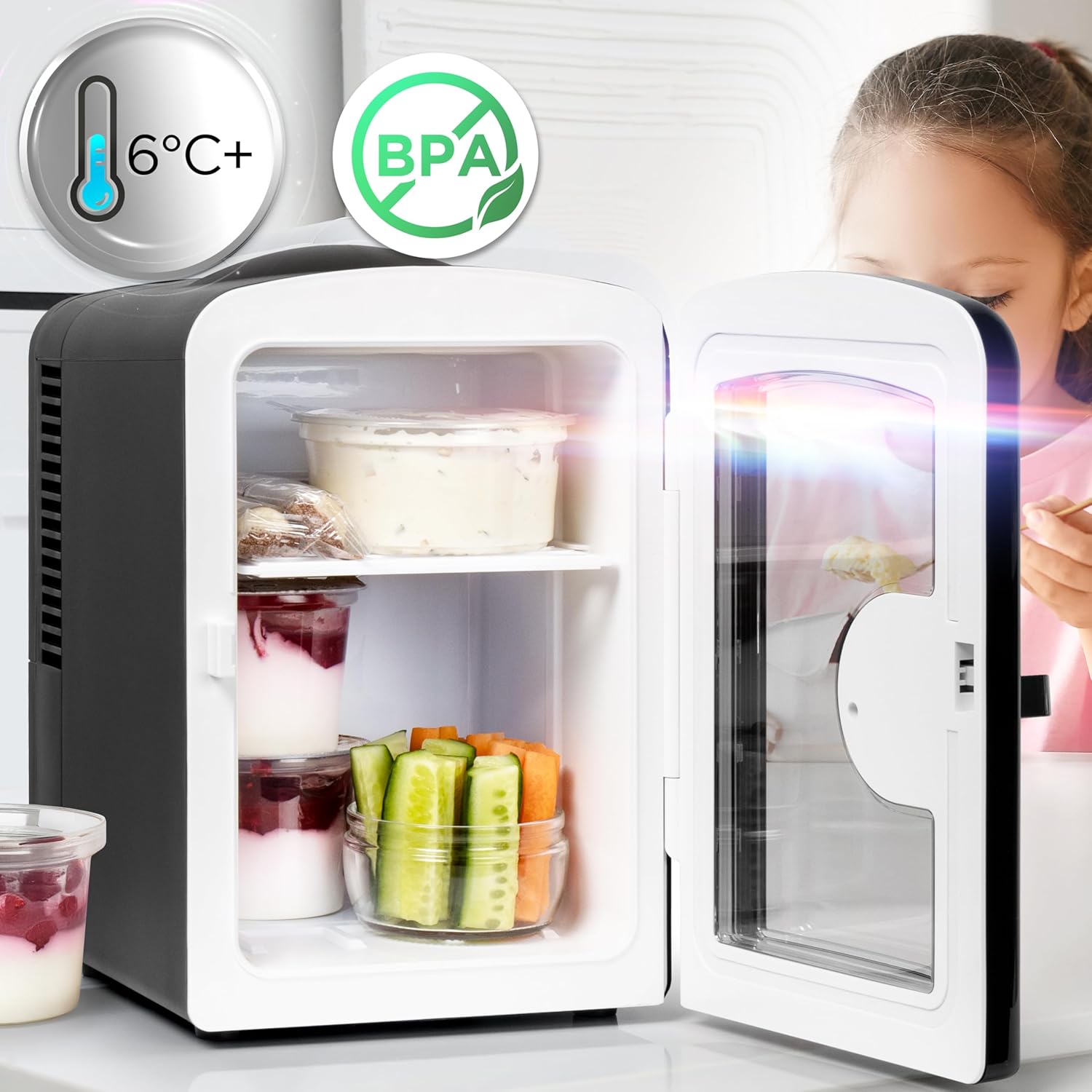 Duronic MFW4 BK Mini Nevera 4L 42W Frigorífico Portátil Mostrando la mini nevera con la puerta abierta y su interior organizado con recipientes de alimentos, yogures y vegetales, destacando en la parte superior sellos informativos de temperatura de 6°C+ y certificación libre de BPA, mientras una persona se encuentra al fondo